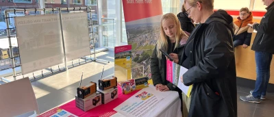 Twee mensen bekijken informatie op een tafel met brochures en promotiemateriaal.