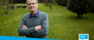 Een man in een groen vest staat met gekruiste armen in een tuin.