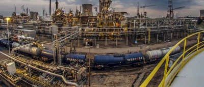 Groot industrieel complex met pijpen en opslagtanks onder een bewolkte lucht.