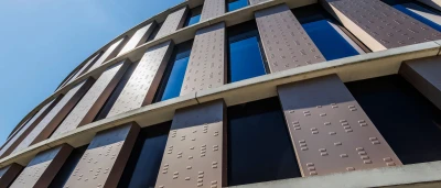 Moderne gevel van een rond gebouw met grote ramen en een heldere blauwe lucht.