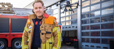 Brandweerman poseert voor de kazerne met een drone op de achtergrond.