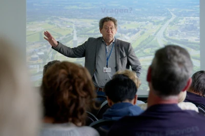 Een man geeft een presentatie voor een publiek, met een projectie op de achtergrond.