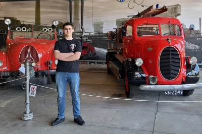 Jongeman staat tussen twee klassieke rode brandweerwagens in een museumsetting.