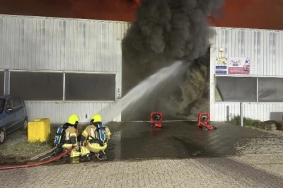 Brandweermannen blussen een grote brand met veel rook bij een loods