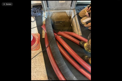 Rode slangen en apparatuur in een open kast, met hand van een persoon zichtbaar.