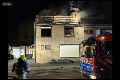 Brandweerman bekijkt een huis met rook en vuur op het dak, brandweerwagen staat dichtbij.