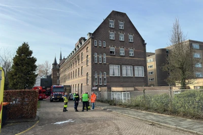 Groep mensen in veiligheidshesjes bij een groot gebouw onder een blauwe lucht.