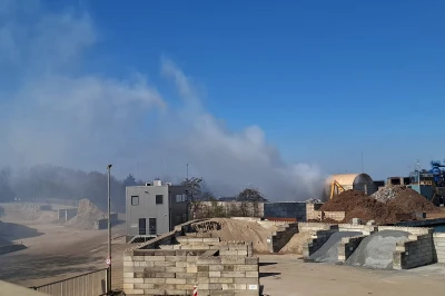Rook stijgt op boven een industrieterrein onder een blauwe lucht.