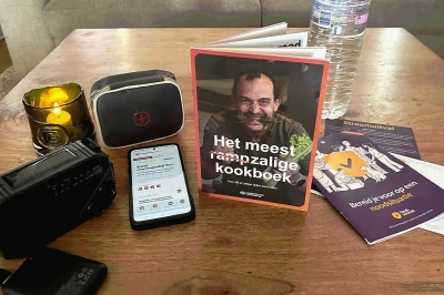 Een kookboek, smartphone en accessoires op een houten tafel met een kaars.