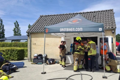 Brandweerlieden verzamelen voor een tent bij een gebouw onder blauwe lucht.