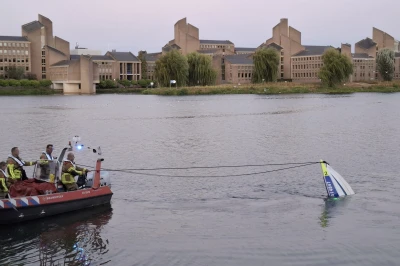 Brandweerboot met team met de gezonken boot aan de kant van het water, gebouwen op de achtergrond.