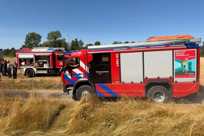 Twee brandweerwagens staan op een landelijke weg tussen hoge, gele grasvelden.