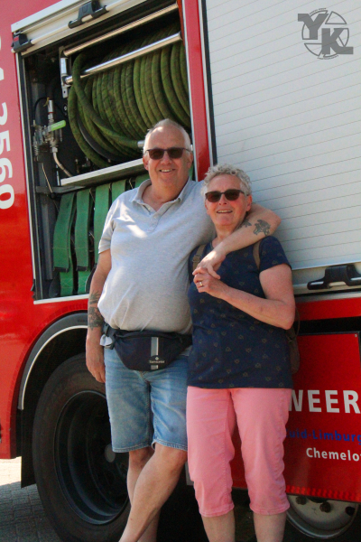 Een man en een vrouw staan naast een brandweerwagen, lachend en ontspannen.