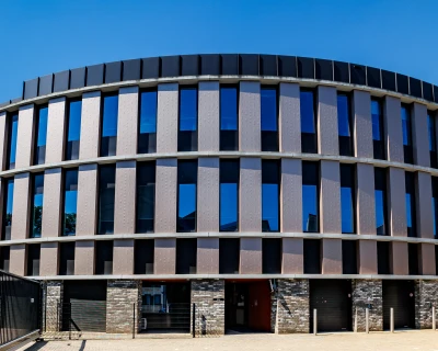 Modern, rond gebouw met veel glas en een stenen fundament onder een blauwe lucht.