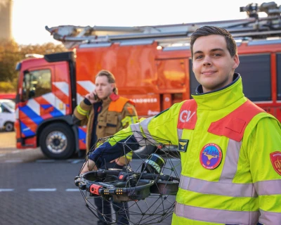Een brandweerman met een drone poseert voor een brandweerwagen.
