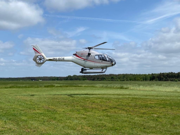 Een witte helicopter zweeft boven een groene veld onder een blauwe lucht.