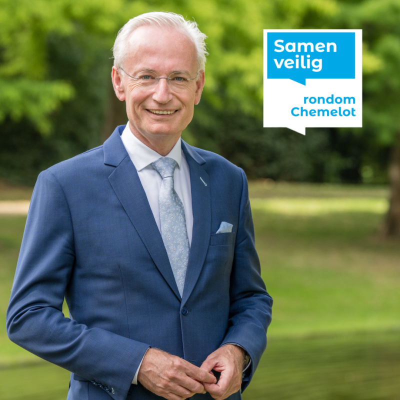 Burgemeester Sittard-Geleen in blauw pak staat glimlachend in een groene parkachtige omgeving.